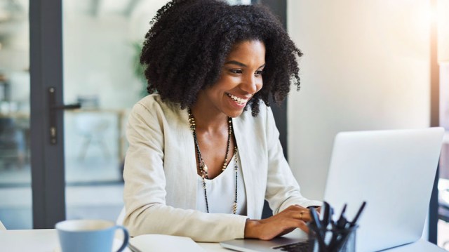 Woman working on a laptop smiling and feeling safe working online because of cybersecurity measures her business has taken